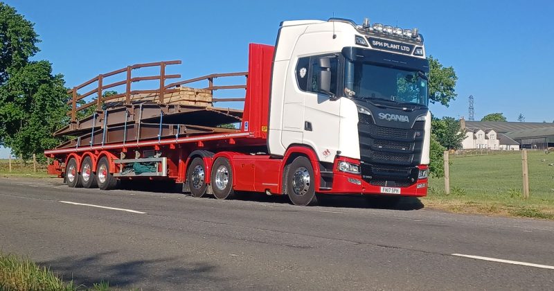 Lorry carrying a bridge parked at the side of a road by a farm