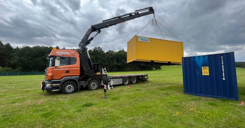 a truck lifting up a yellow storage container next to a blue one