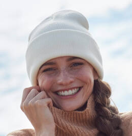Woman modelling a white beanie while smiling cheek to cheek